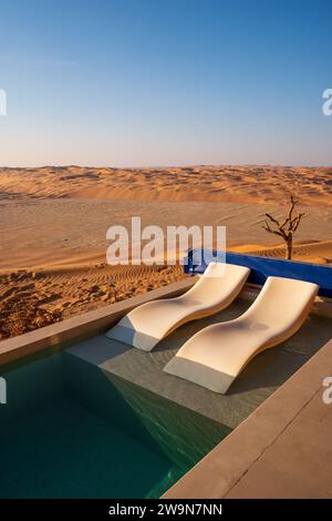 Piscine privée et chaises longues sur fond de dunes de sable et de paysage désertique. Soleil éclatant, quartier vide, Abu Dhabi, émirats arabes unis Banque D'Images