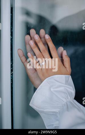 le romantisme des mains de deux couples pressées contre le verre. La main de la femme porte une bague de mariage et une robe blanche, tandis que la main de son partenaire l'est Banque D'Images