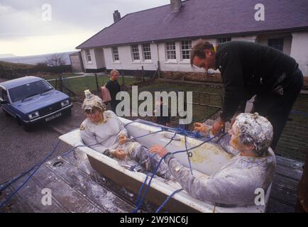 Noircir la mariée et le marié 1980s Écosse. Un rituel de mariage écossais folklorique pré-mariage. Un jeune couple est conduit à travers la ville attaché assis dans une baignoire à l'arrière d'un camion. Ils sont recouverts de farine et d'œufs. Ce rituel pré-mariage a lieu la veille de leur mariage et est connu comme «noircissement» ou reschtach, et apparemment éloigner les mauvais esprits avant le mariage. Mallaig, Écosse 1980s 1987 Royaume-Uni HOMER SYKES Banque D'Images