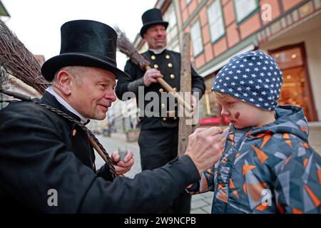 Wernigerode, Allemagne. 29 décembre 2023. Karl, quatre ans, reçoit une partie de la suie des rameaux Thomas Schramm (l) et Gabor Mäntz. L'équipe de ramoneurs se rend régulièrement dans les montagnes du Harz avant le réveillon du nouvel an pour porter chance. Les ramoneurs sont considérés comme des charmes chanceux depuis des siècles. L'atlas du bonheur de la SLK pour 2023 montre que la Saxe-Anhalt est l'État le mieux placé de l'Allemagne de l'est. Au niveau national, la Saxe-Anhalt occupe la sixième place. Crédit : Matthias Bein/dpa/ZB/dpa/Alamy Live News Banque D'Images