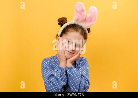 Portrait de jolie mignonne fille de préadolescence enfant portant des oreilles de lapin rose, heureux regardant l'appareil photo, posant isolé sur le backgro de couleur jaune Uni Banque D'Images