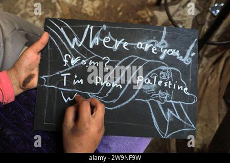 Rafah. 28 décembre 2023. Un étudiant écrit "Je suis de Palestine" dans une salle de classe temporaire dans la ville de Rafah, dans le sud de la bande de Gaza, le 28 décembre 2023. Certains étudiants de Gaza sont passés étudier dans des salles de classe temporaires car de nombreuses écoles sont utilisées ici pour accueillir les sans-abri infligés par une nouvelle vague de conflit israélo-palestinien. Crédit : Rizek Abdeljawad/Xinhua/Alamy Live News Banque D'Images