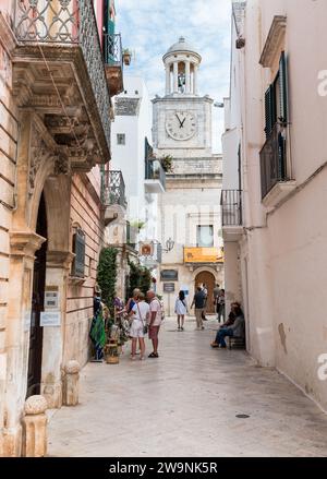 Locorotondo, Pouilles, Italie - 5 octobre 2023 : rue étroite avec vue sur la Tour de l'horloge dans le centre de Locorotondo, ville métropolitaine de Bari. Banque D'Images