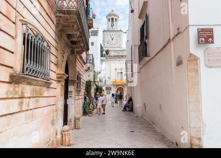 Locorotondo, Pouilles, Italie - 5 octobre 2023 : rue étroite avec vue sur la Tour de l'horloge dans le centre de Locorotondo, ville métropolitaine de Bari. Banque D'Images