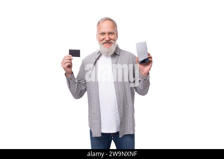 un bel homme retraité avec une barbe et une grosse moustache vêtu d'une chemise et d'un jean tient une maquette de carte en plastique et un smartphone avec l'écran Banque D'Images