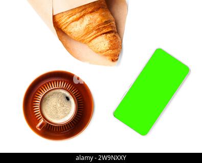 Plat de tasse brune de café noir avec croissant et téléphone. Croissant enveloppé dans du papier artisanal, téléphone avec écran vert (chromakey), objets isolent Banque D'Images