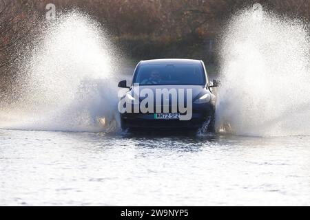 Une voiture électrique vue faire un grand éclaboussure alors qu'elle voyage à travers une route inondée à Fairburn, North Yorkshire, Royaume-Uni Banque D'Images