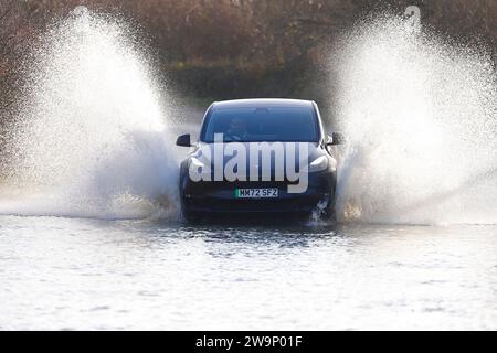 Une voiture électrique vue faire un grand éclaboussure alors qu'elle voyage à travers une route inondée à Fairburn, North Yorkshire, Royaume-Uni Banque D'Images