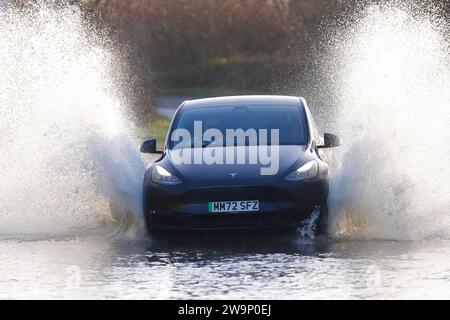 Une voiture électrique vue faire un grand éclaboussure alors qu'elle voyage à travers une route inondée à Fairburn, North Yorkshire, Royaume-Uni Banque D'Images