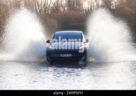 Une voiture électrique vue faire un grand éclaboussure alors qu'elle voyage à travers une route inondée à Fairburn, North Yorkshire, Royaume-Uni Banque D'Images