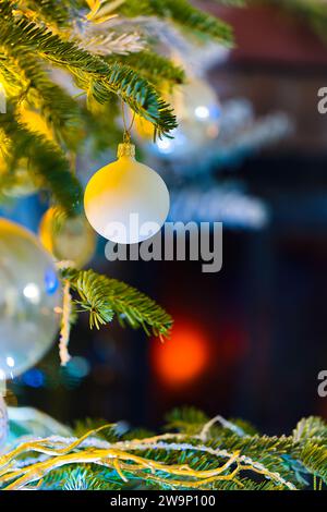 Plongez dans l'esprit des fêtes avec cette photo enchanteresse représentant des boules sur un sapin caucasien. Des lumières de Noël floues et un décor festif rehaussent le décor Banque D'Images