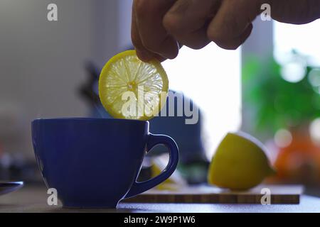 Un homme âgé tient une tranche de citron sur une tasse de thé dans la cuisine Banque D'Images