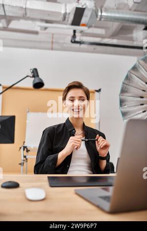 jolie femme joyeuse aux cheveux courts en tenue décontractée travaillant en studio et ayant beaucoup de plaisir Banque D'Images