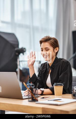 photographe féminine heureuse et attrayante dans une tenue décontractée ayant un appel vidéo et souriant joyeusement Banque D'Images