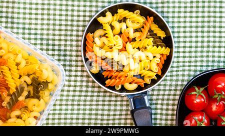 Petite petite poêle à frire avec pâtes fusilli crues tricolores dans une composition rustique. Banque D'Images