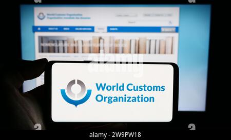 Personne détenant un téléphone cellulaire avec le logo de l'Organisation mondiale des douanes (OMD) devant la page Web. Concentrez-vous sur l'affichage du téléphone. Banque D'Images