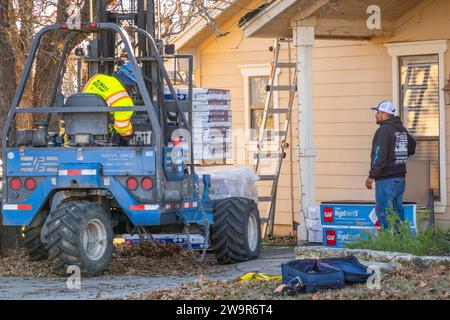 Deux travailleurs déchargeant des bardeaux de toiture en asphalte du chariot élévateur pour le remplacement du toit Banque D'Images