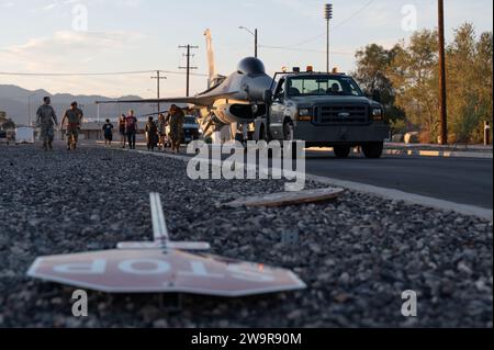 Des aviateurs américains affectés au 57e Escadron de maintenance d'aéronefs et au 99e escadron du génie civil transportent un F-16 Fighting Falcon à la base aérienne de Nellis, Nevada, le 21 juin 2023. Tout en guidant l’avion, des aviateurs ont enlevé plusieurs panneaux de signalisation pour faire de la place à l’envergure du F-16. (Photo de l'US Air Force par Airman 1st Class Jordan McCoy) Banque D'Images