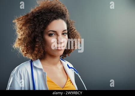 Médecin aux cheveux bouclés, en tenue clinique, affiche une détermination subtile dans son regard régulier Banque D'Images