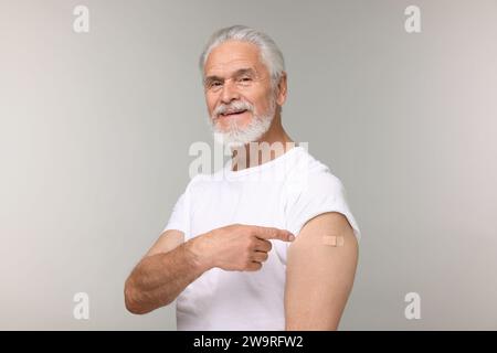 Homme âgé pointant le pansement adhésif après vaccination sur fond gris clair Banque D'Images