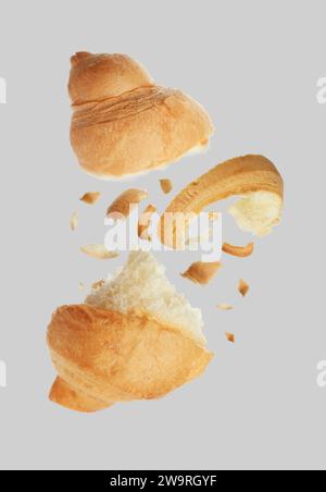 Morceaux de délicieux croissant frais tombant sur fond gris Banque D'Images