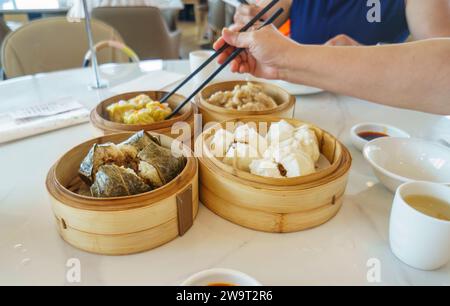 Yumcha, dim sum dans les cuiseurs à vapeur en bambou. Mains tenant des baguettes. Mise au point sélective sur les steamers au premier plan. Cuisine chinoise. Banque D'Images