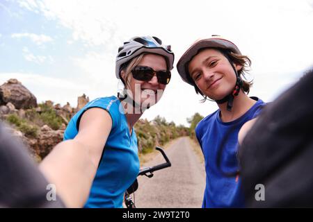 Joyeux mère et fils cycliste prenant selfie contre le ciel nuageux à l'extérieur Banque D'Images