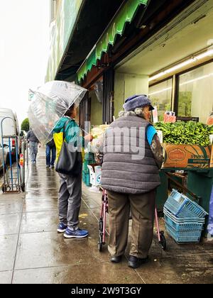 Deux femmes faisant des courses sous la pluie dans un marché extérieur à Chinatown, San Francisco, Californie Banque D'Images