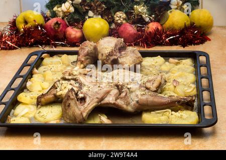 Agneau fraîchement rôti et pommes de terre sur une plaque de cuisson, encadrés par des fruits frais et des décorations de vacances. Nourriture de Noël radiationnelle. Banque D'Images