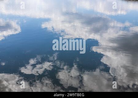 Surface d'eau calme. Soir d'été près d'un lac forestier, la surface de l'eau est lisse, avec de petites vagues. Le ciel avec des nuages est réfléchi par le Banque D'Images