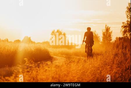 Cycliste sur un vélo de gravier roulant sur un sentier poussiéreux dans un champ au coucher du soleil. Mise au point sélective. Banque D'Images