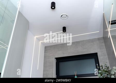 Bandes lumineuses LED montées dans le mur et le plafond dans une salle de bain moderne, anemostat de ventilation visible. Banque D'Images