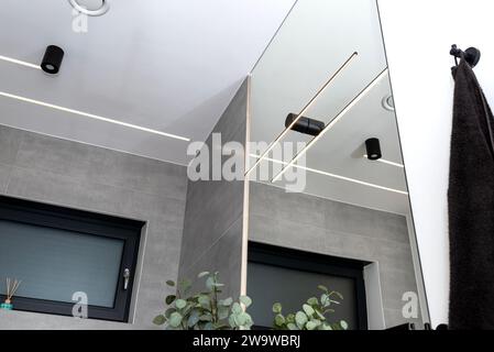 Bandes lumineuses LED montées dans le mur et le plafond dans une salle de bain moderne, anemostat de ventilation visible. Banque D'Images