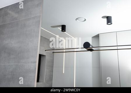 Bandes lumineuses LED montées dans le mur et le plafond dans une salle de bain moderne, anemostat de ventilation visible. Banque D'Images