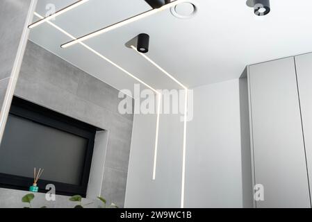 Bandes lumineuses LED montées dans le mur et le plafond dans une salle de bain moderne, anemostat de ventilation visible. Banque D'Images