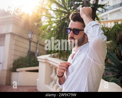 Mode de plein air pour jeunes adultes élégant avec lunettes de soleil et barbe. Photo d'un homme élégant portant des lunettes de soleil et une chemise blanche croustillante. Banque D'Images