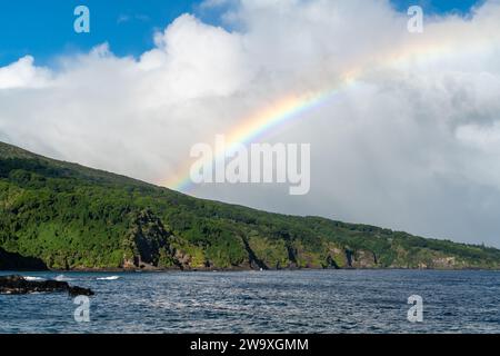 Un arc-en-ciel brillant s'étend dans le ciel au-dessus des falaises côtières du parc national de Haleakalā, vu de la route Piilani à Maui. Banque D'Images