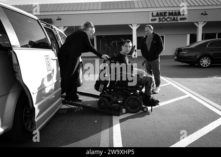 Longwood, Floride, États-Unis. 29 décembre 2023. Allison et Joe Holmes avec un fils handicapé JJ quittent sa fourgonnette adaptée pour une brève sortie.JJ, 19 ans, souffre de paralysie cérébrale et est incapable de prendre soin de lui-même. Il parle à travers son clavier iPad qu'il contrôle en utilisant son nez pour taper, et malgré ses nombreux défis fréquente un collège communautaire où il étudie les sciences politiques. « C’est la politique qu’il aime, et c’est aussi sa frustration majeure », note sa mère Allison. Jj has.been sur la liste d'attente de l'État pour le soutien de la renonciation Medicaid pendant 17 ans, et a rencontré plusieurs délégations de législateurs de l'État Banque D'Images