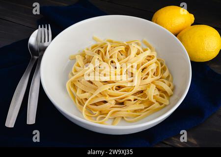 Fettuccine à la sauce citron-mascarpone dans un bol à pâtes : nouilles larges servies dans un bol peu profond et garnies de zestes de citron Banque D'Images