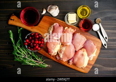 Cuisses de poulet au romarin avec sauce aux canneberges Ingrédients : cuisses de poulet crues, romarin frais, jus de canneberges, et plus sur une table en bois foncé Banque D'Images