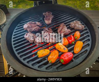 Un barbecue de type oeuf kamado debout sur une terrasse de la maison de séjour avec un steak d'aloyau de bœuf, filet mignon et légumes à cuire sur feu ouvert Banque D'Images