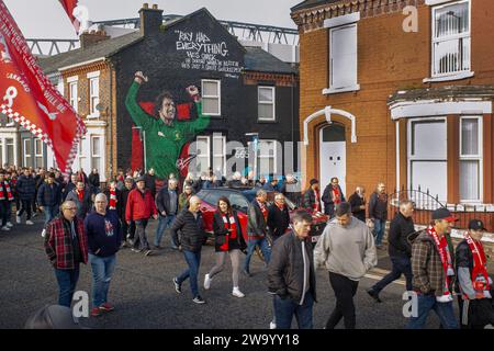 Les supporters du Liverpool FC passent devant une fresque à Anfield avec le stade en arrière-plan. Banque D'Images