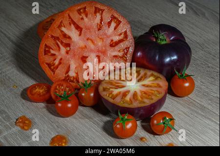 Un groupe de tomates, une grosse coupe rose en deux face à la photo, une autre coupe bleue entière et une demi bleue face vers le haut avec d’autres petites tomates cerises Banque D'Images