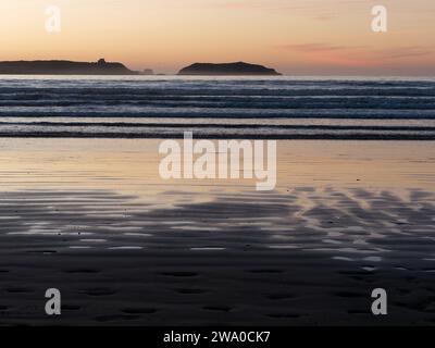 Coucher de soleil sur une île à Essaouira alors que les vagues roulent vers une plage de sable et la lumière orange se reflète dans l'eau. Maroc. 31 décembre 2023 Banque D'Images