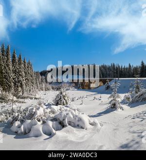 Viaduc de pierre (pont d'arche) sur le chemin de fer à travers la forêt de sapins enneigés de montagne. La neige dévie sur le côté de la voie et le givre sur les arbres et les fils électriques. Banque D'Images