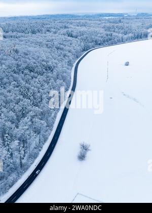 Une route sinueuse traverse un paysage hivernal avec des champs enneigés, vue aérienne, Gechingen, Forêt Noire, Allemagne, Europe Banque D'Images