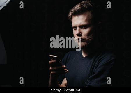 Bel homme barbu élégant tenant un smartphone dans ses mains et regardant l'appareil photo, concept de brutalité et de solitude Banque D'Images