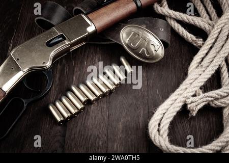 Old West gun - fusil à répétition à levier avec cartouches et boucle en bronze US Army marquée sur une table en bois Banque D'Images