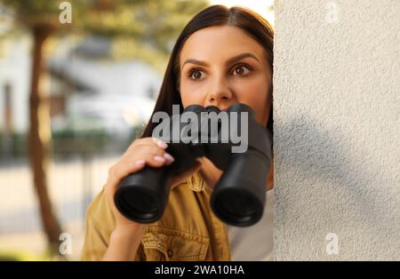 Concept de vie privée. Curieuse jeune femme avec des jumelles espionnant les voisins à l'extérieur Banque D'Images