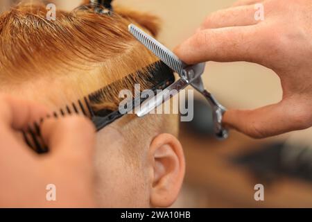 Coiffeur professionnel coupant les cheveux de garçon dans le salon de beauté, closeup Banque D'Images